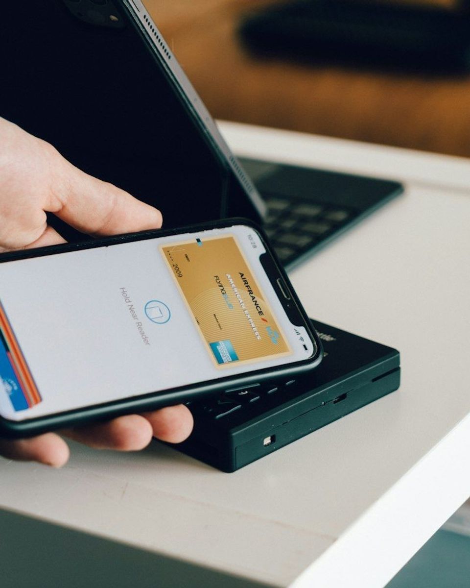 A person holding a smartphone over a card reader for contactless payment