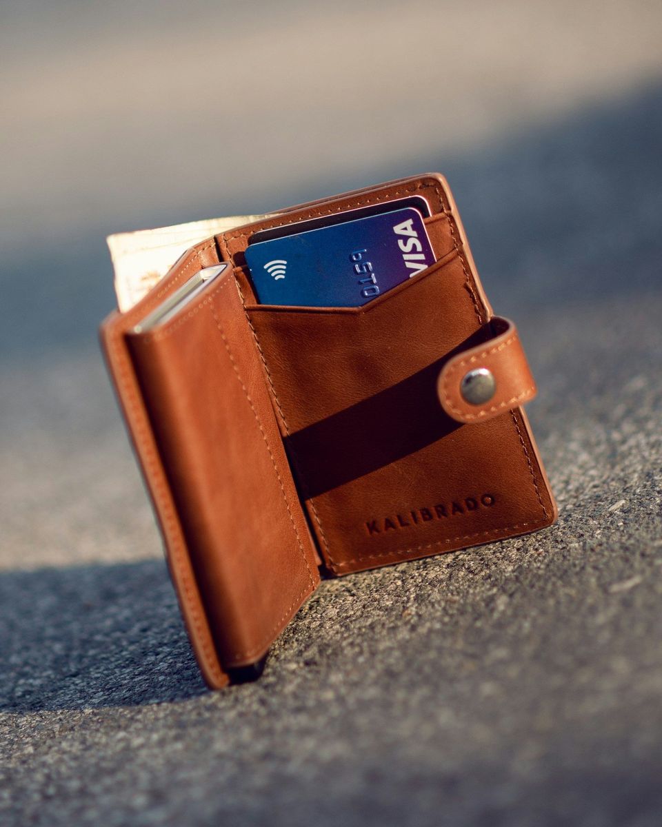 A brown leather bifold wallet on a concrete floor
