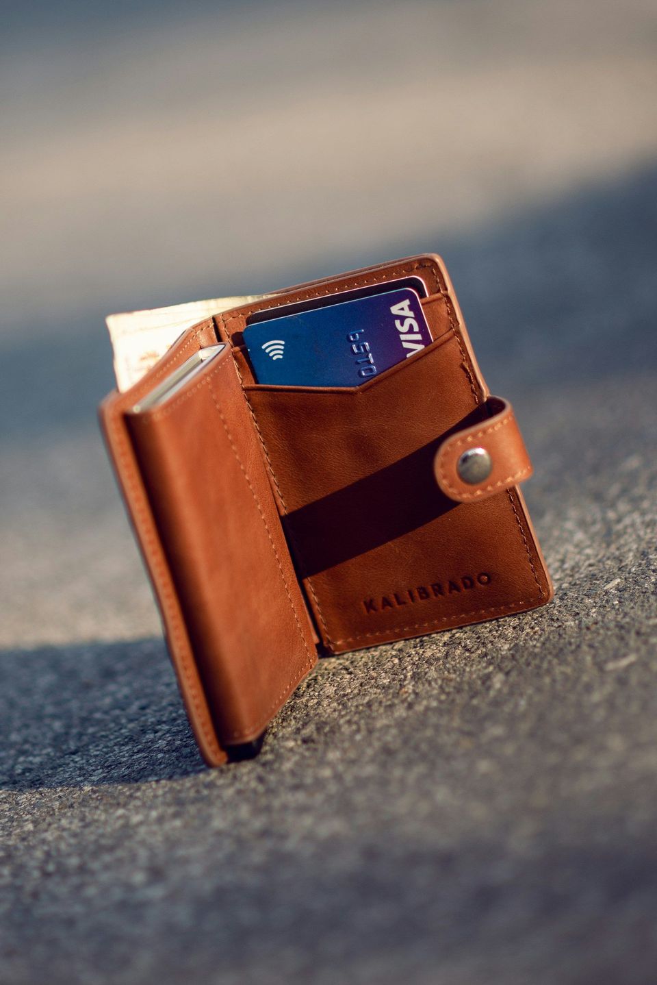 A brown leather bifold wallet on a concrete floor